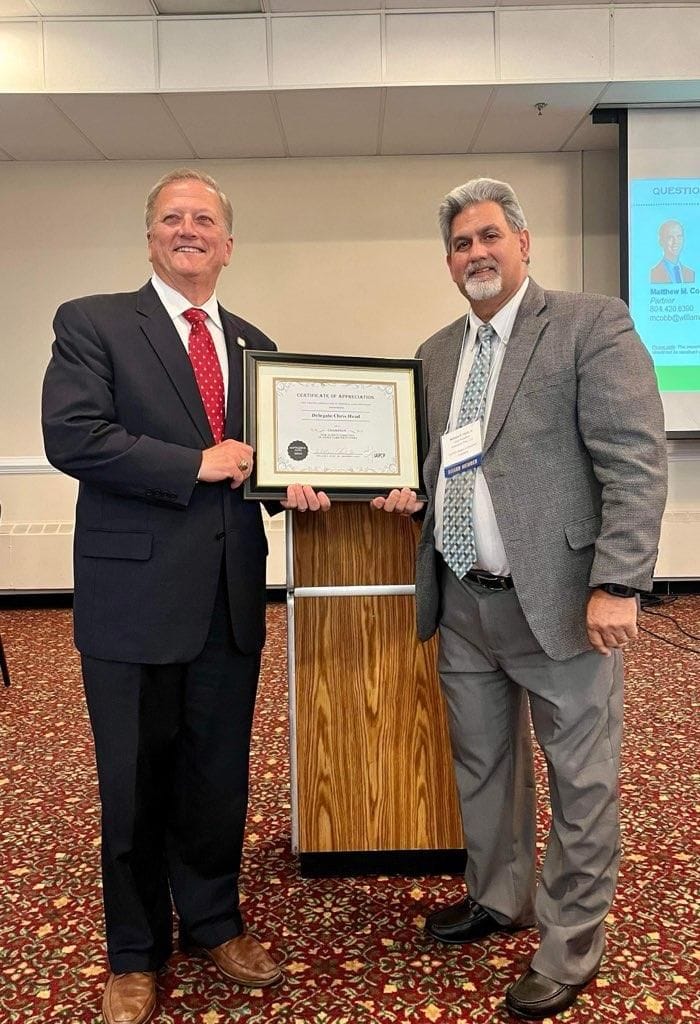 Two men at a conference podium holding a framed Certificate of Appreciation presented to Delegate Chris Head