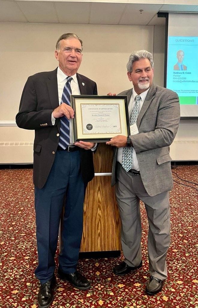 Two men at a conference podium holding a framed Certificate of Appreciation presented to Senator Emmett Hanger
